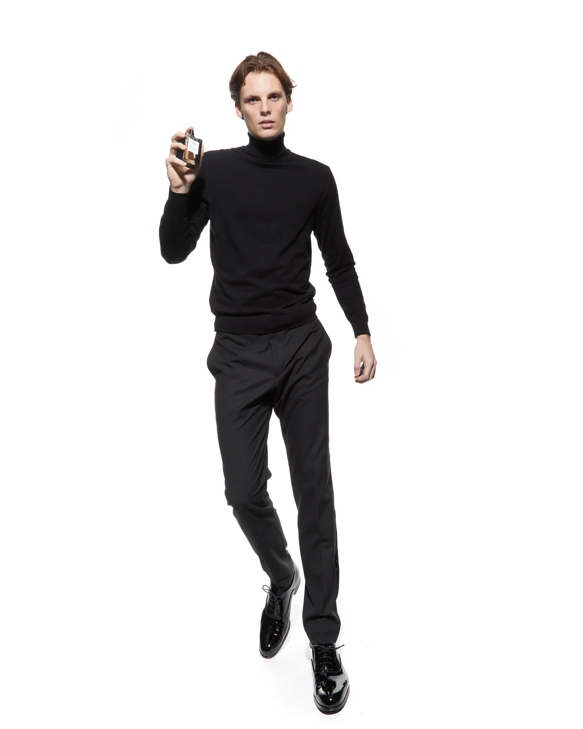 Man wearing a black turtleneck and pants holding a bottle of Verset Perfume on a white background
