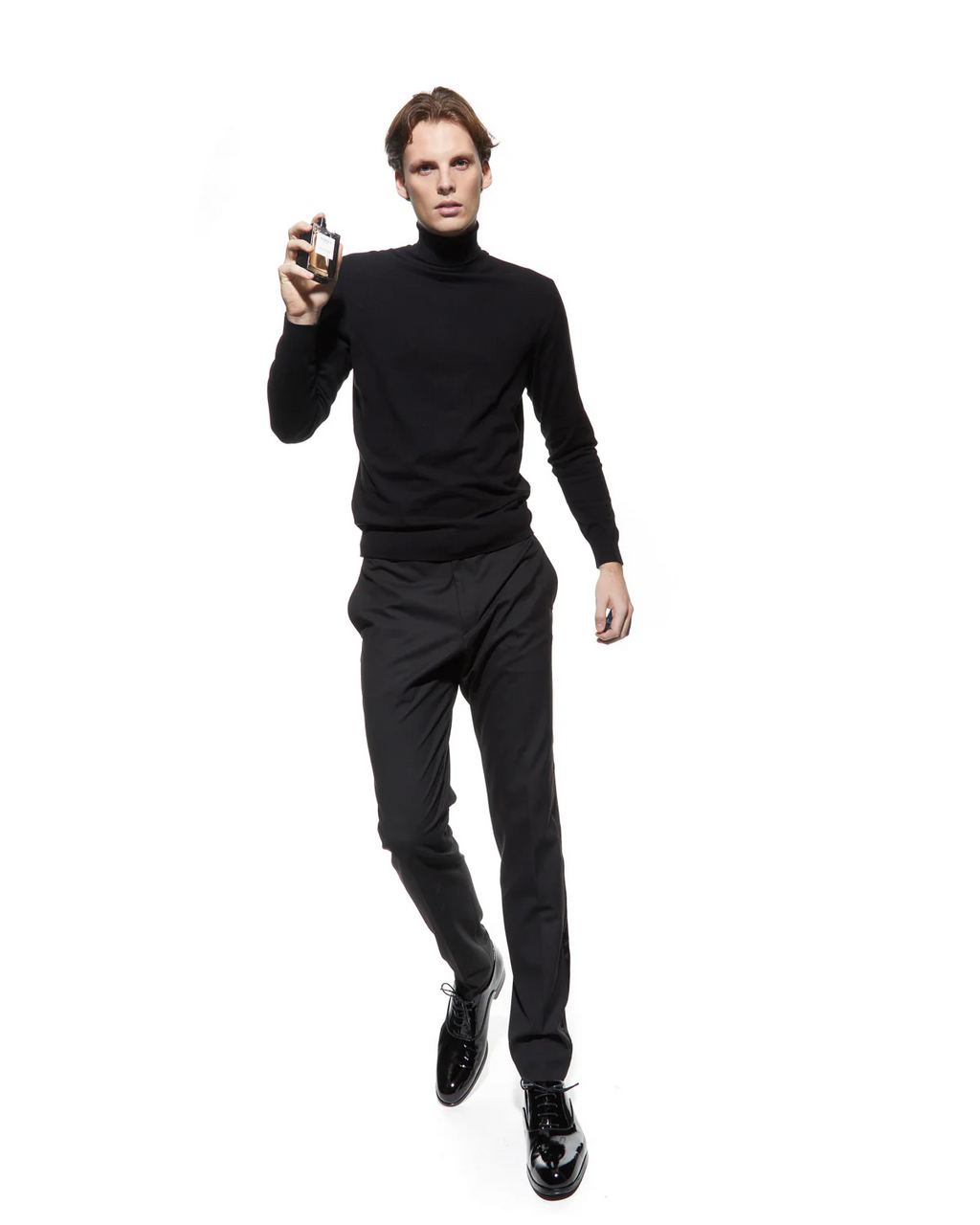 Man wearing a black turtleneck and pants holding a bottle of Verset Perfume on a white background